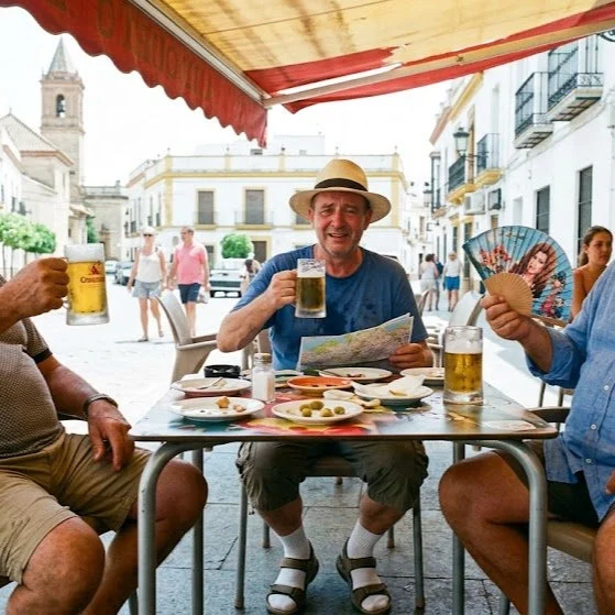 Turista a 48 Grados a La Sombra...(Relato De Humor)
En un Lugar de Andalucía, el termómetro del salpicadero marcaba 48 grados a la sombra y en la plaza del pueblo no había sombra alguna. En la puerta del bar El Chiringuito, sentados en dos sillas de plástico blanco ajustadas milimétricamente debajo del único pedacito de sombra que proyectaba un toldo a punto de jubilarse, estaban Paco y El Primo. Ninguno de los dos se había movido en tres horas para no gastar saliva ni provocar corrientes de aire innecesarias.
—Paco —dijo El Primo, agitando levemente un abanico con la cara de Rocío Jurado.
—Dime, Primo. Respondió Paco.
—Hace una jartá de calor, ¿no?
—Algo se nota, —respondió Paco sudando a mares. Pero parece que quiere refrescar respecto al martes pasado, que cayeron dos gorriones fritos del cielo.
En ese momento pasó por la calle un turista despistado, vestido con calcetines blancos hasta las rodillas, sandalias y un sombrero de paja que no engañaba a nadie. Se detuvo frente a ellos sudando a chorros y sacó un mapa de papel que ya parecía una servilleta mojada.
—Disculpen —dijo el hombre con acento del norte—. ¿Saben si falta mucho para la catedral?
—¿Para la catedral? —Paco miró a El Primo y luego al reloj del campanario, que marcaba las cuatro de la tarde. Caballero, a esta hora la catedral está cerrada y el cura está en el tercer sueño de su siesta diaria. Si sigue andando en esa dirección a estas horas, la única catedral que va a ver es la del Juicio Final.
El turista parpadeó, confundido por el diagnóstico médico improvisado.
—Es que quería aprovechar el día —insistió el visitante.
—Mire usted —dijo El Primo, levantando con esfuerzo sagrado un dedo para señalar una silla vacía—. Aprovechar el día aquí a las cuatro de la tarde es llegar con vida a las ocho. Siéntese ahí, pida un tubo de cerveza bien tirado, que no es cerveza, es suero fisiológico, y no se mueva. Si se mueve, la calor lo huele y se lo lleva.
El turista superado por el rigor científico del argumento y con el intenso bochorno ambiental, se dejó caer en la silla de plástico.
A los cinco minutos, Manolo, el dueño del bar, salió a la terraza con una...Sigue en mi Blog.
Rovica.